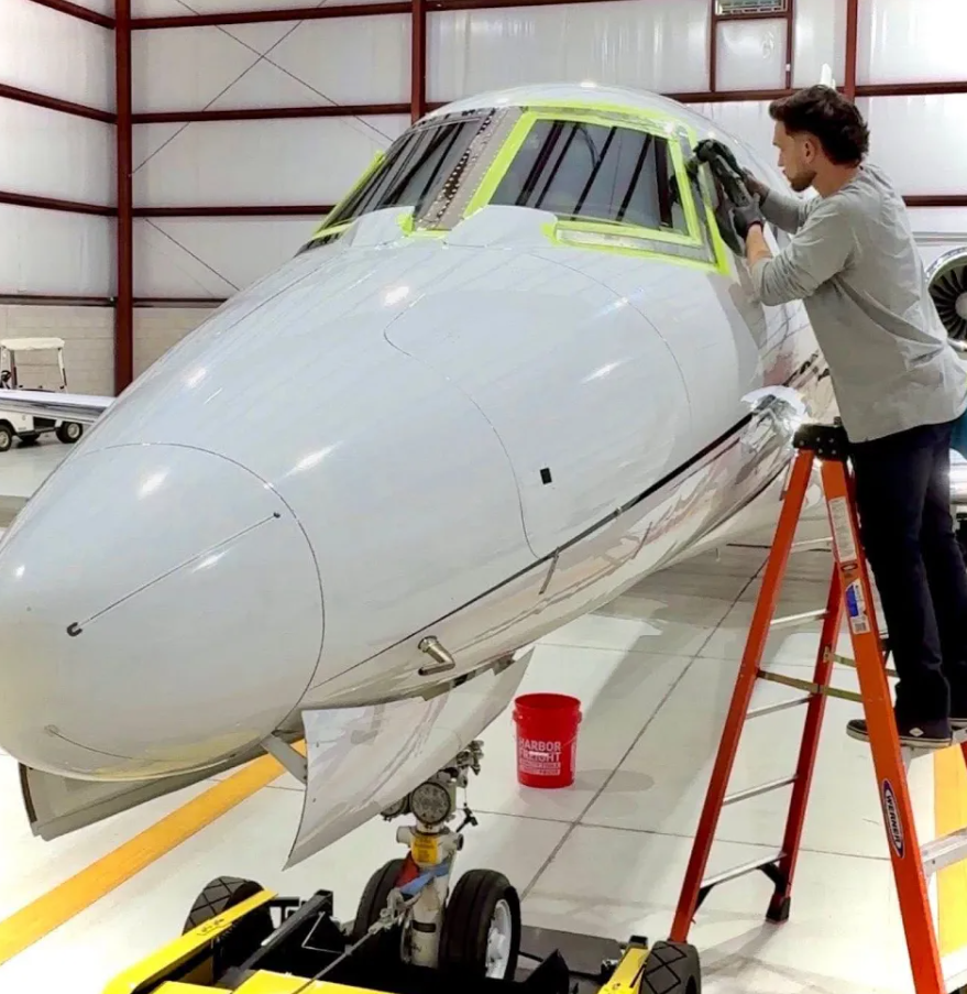 Mitch detailing the cockpit windows of a private jet from a ladder inside a hangar