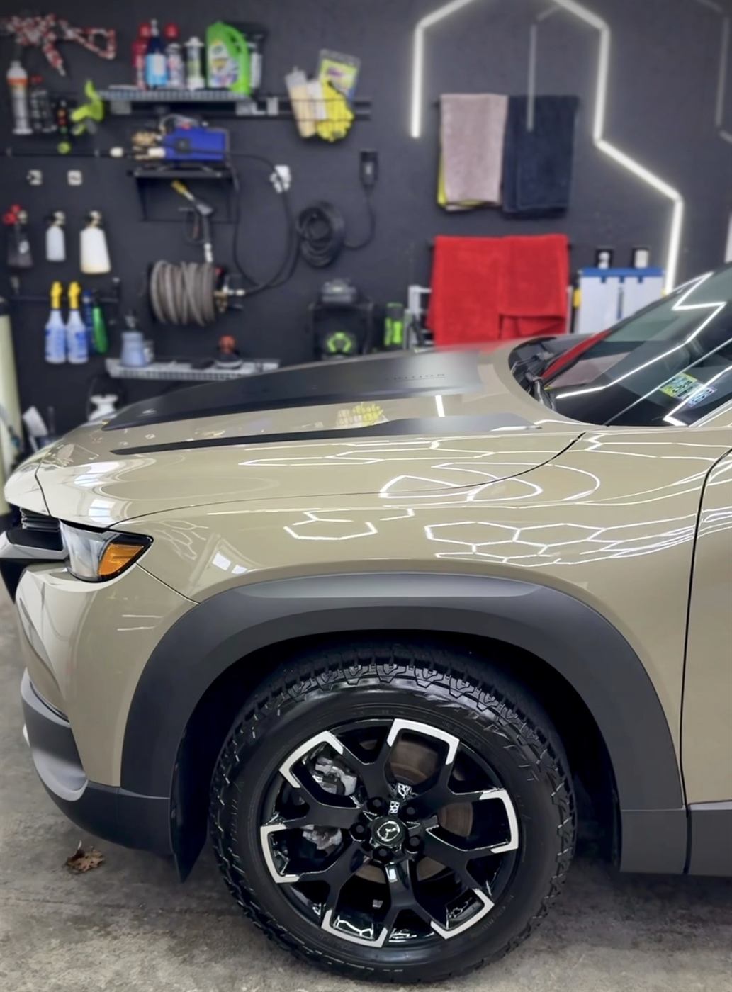 Overhead LED strips reflecting in the polished hood of a tan SUV in the detail bay