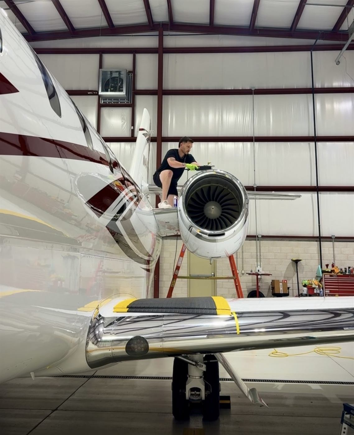 Technician detailing a private jet's engine and tail inside a hangar