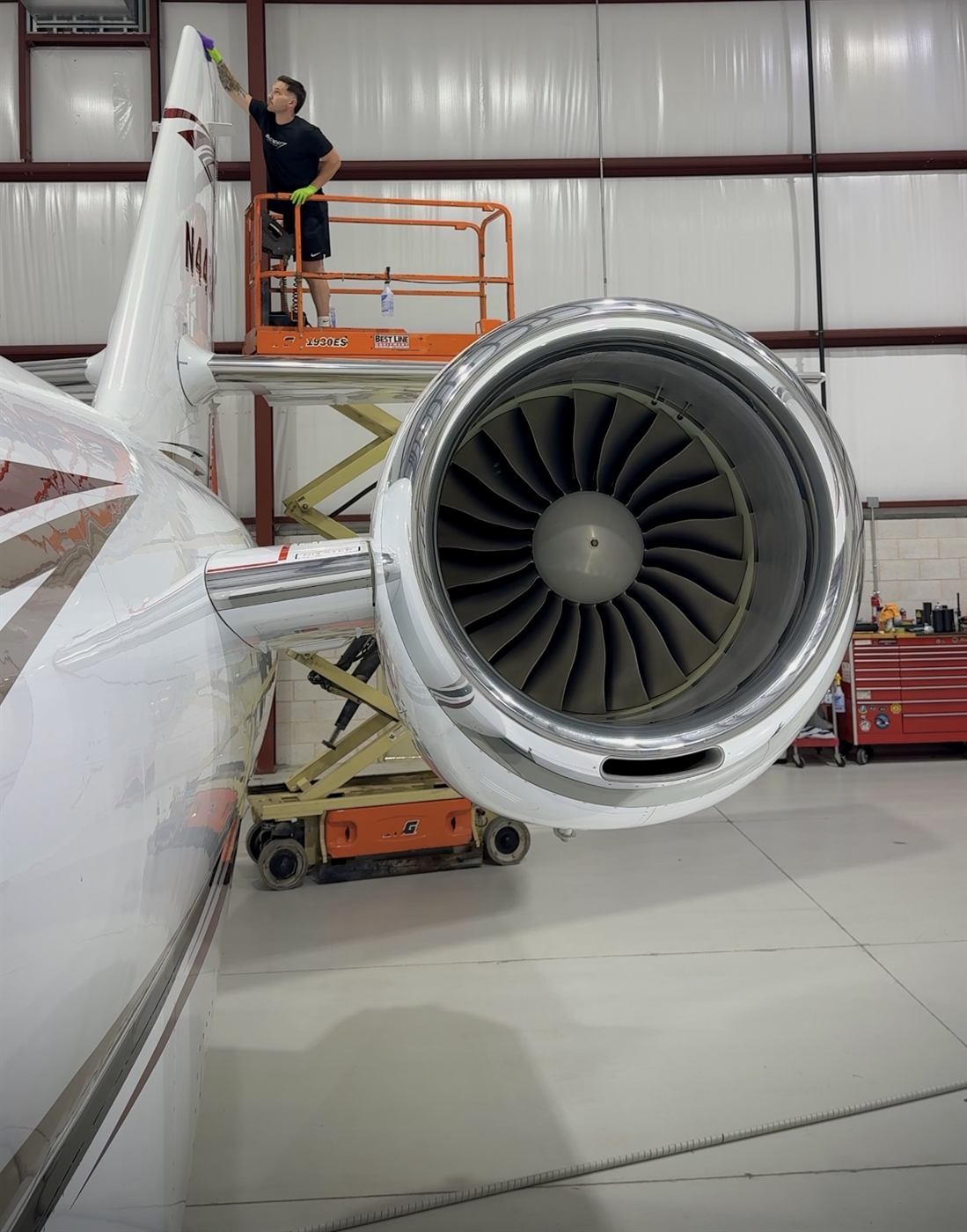 Technician on a lift detailing a private jet's tail beside its engine
